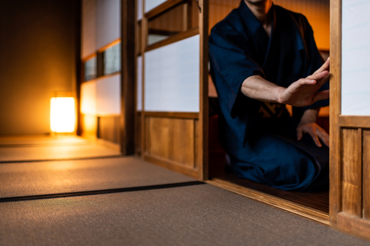 Traditional japanese house or ryokan with man in kimono opening shoji sliding paper doors sitting on tatami mat floor